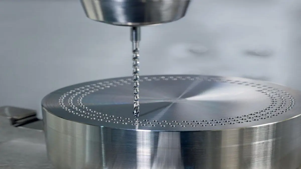 Rotating drill bit creating a pattern of small holes in a round metal block.