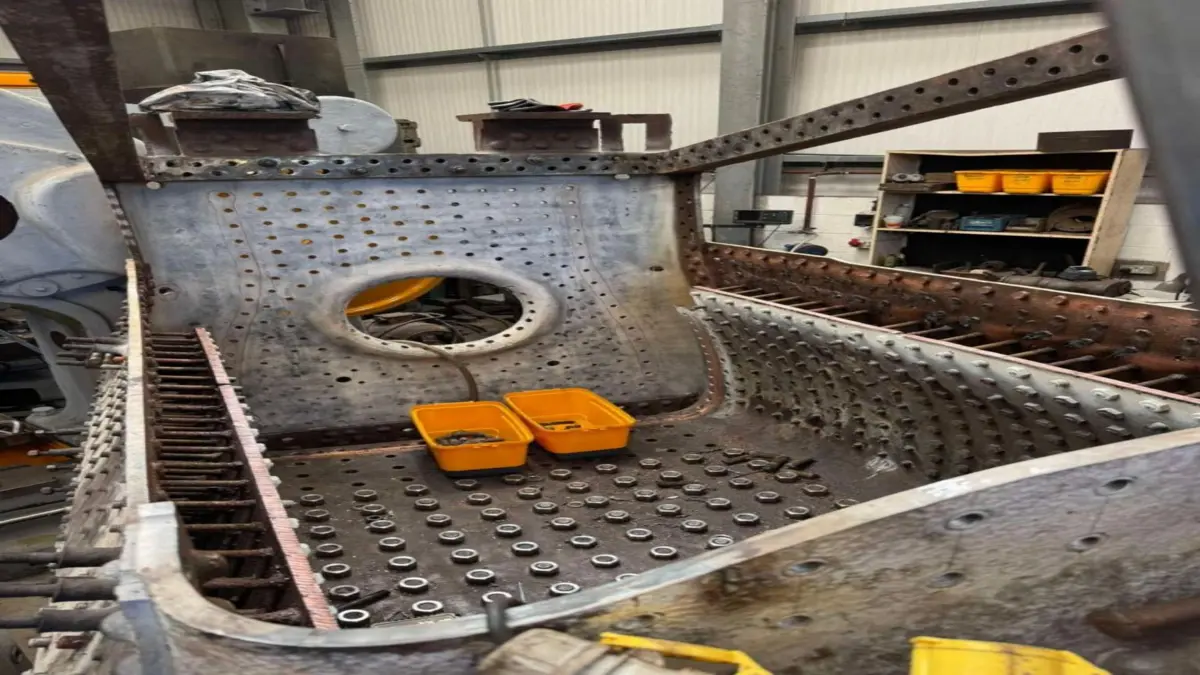 Large metal chamber with numerous small holes, bolts, and two yellow plastic bins inside.