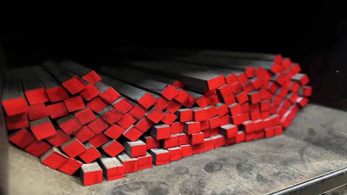 Stack of rectangular steel bars with red-tinted ends arranged on a metal surface.